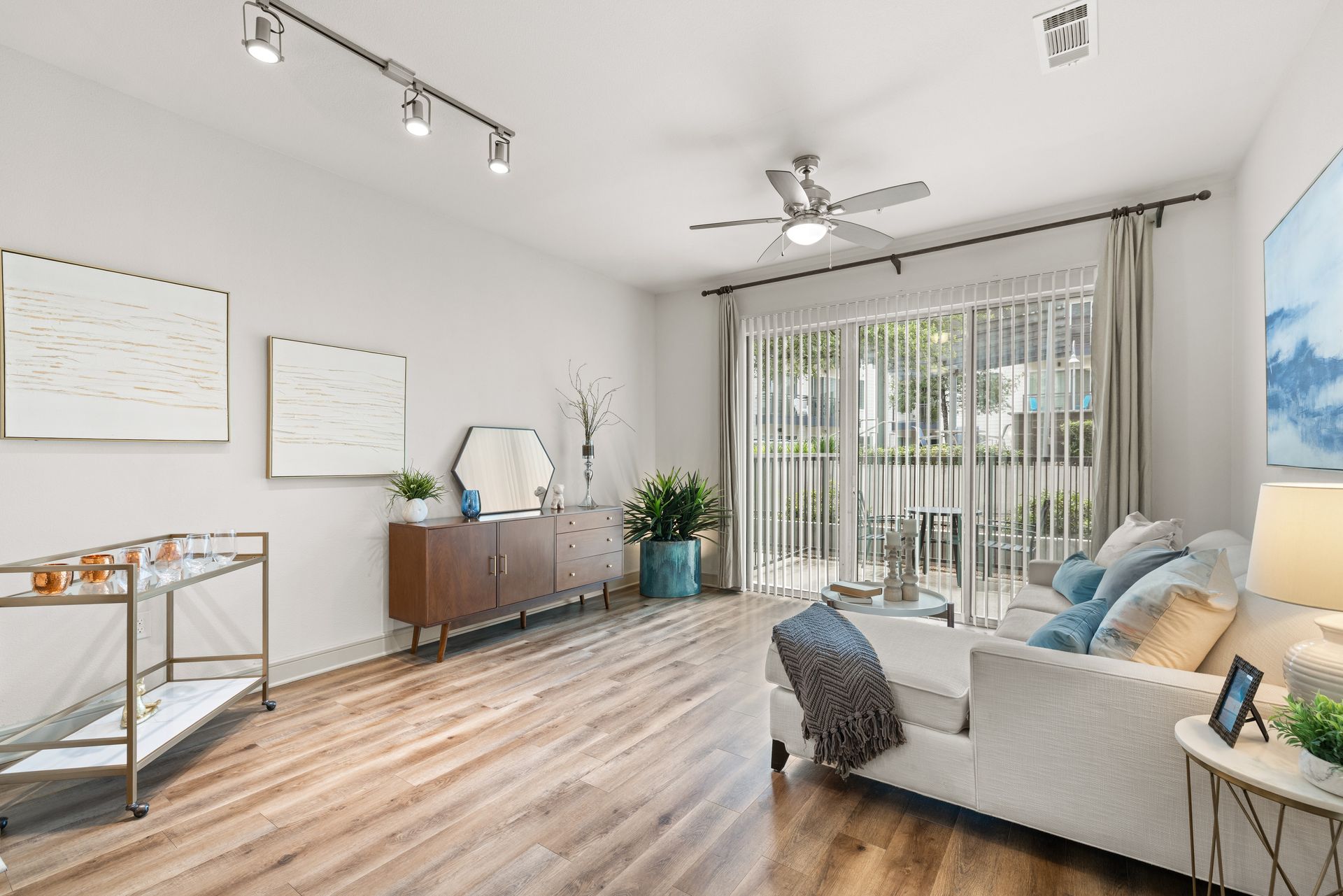 Bright modern living room with sofa, sliding glass doors, wood floor, and ceiling fan at Sabina in Austin, TX.