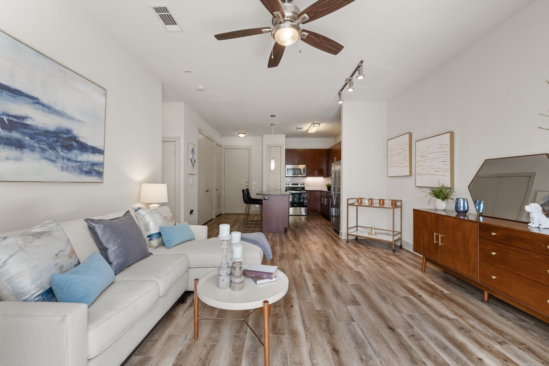 Bright living room with white sofa, round coffee table, wood floors, ceiling fan, and sideboard with decor.