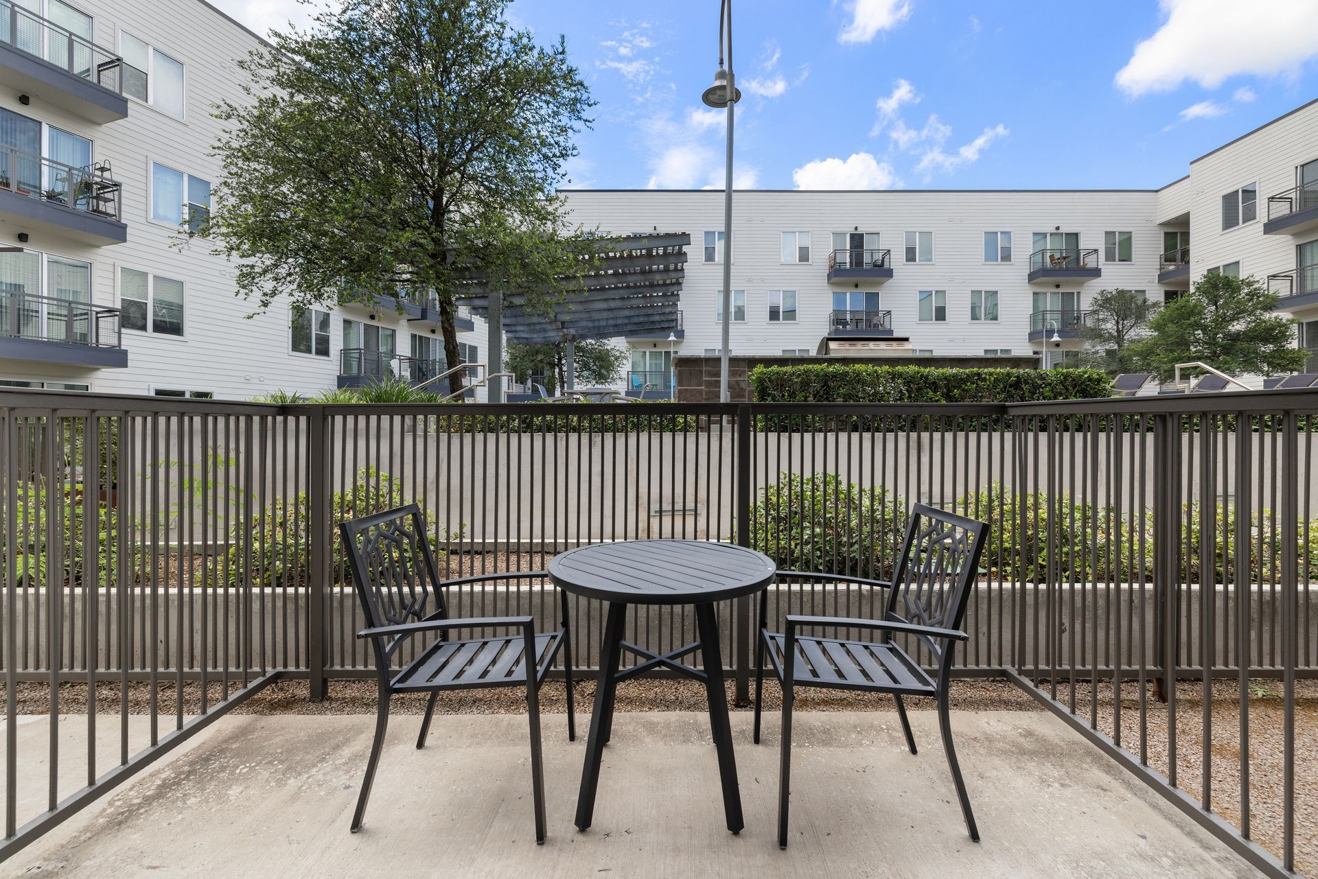 Outdoor patio with black table and two chairs overlooking apartment buildings and a tree at Sabina in Austin, TX.