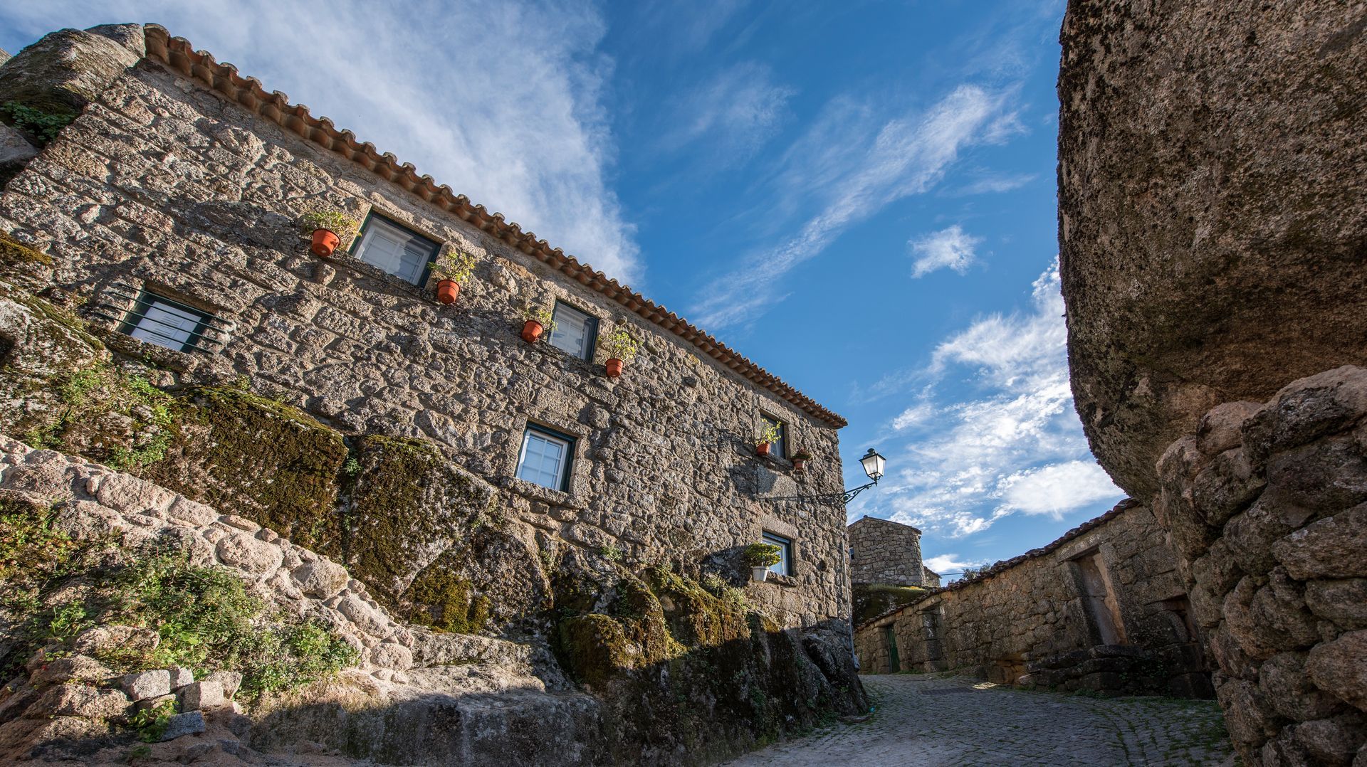 Edifício de pedra ao longo de um caminho estreito sob um céu azul, visto de baixo