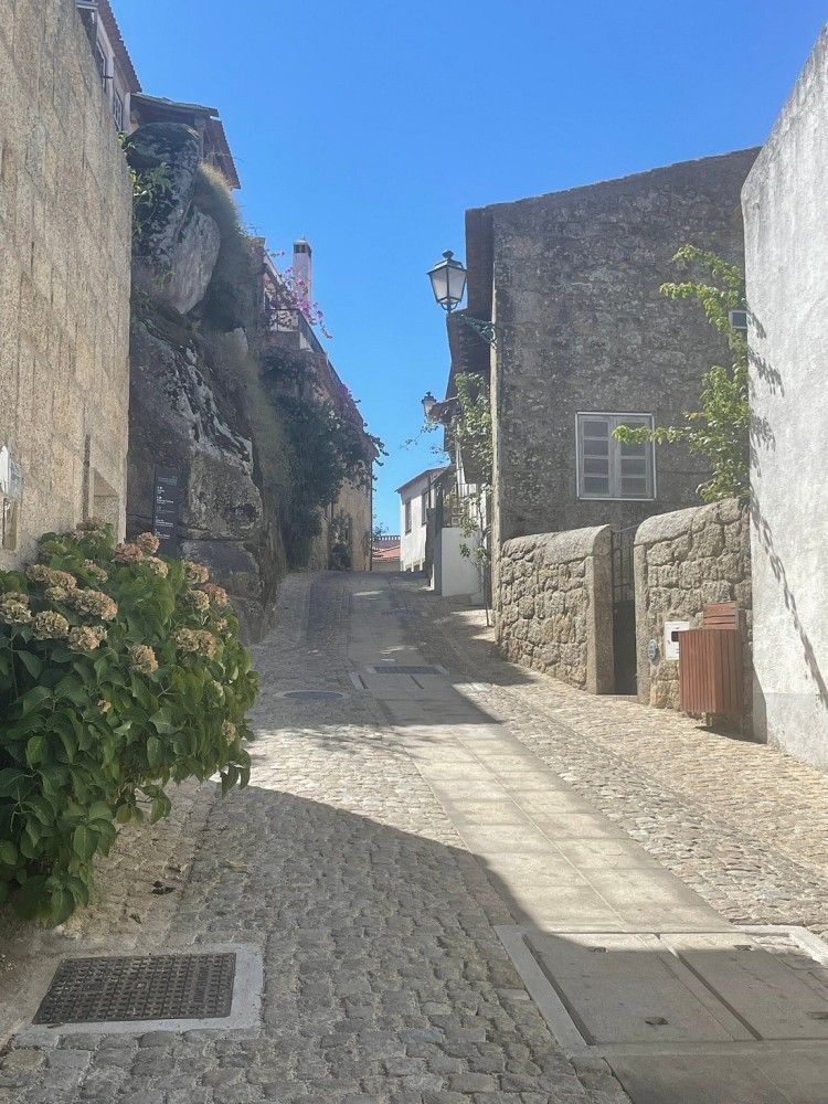 Rua estreita de paralelepípedos ladeada por edifícios de pedra sob um céu azul brilhante