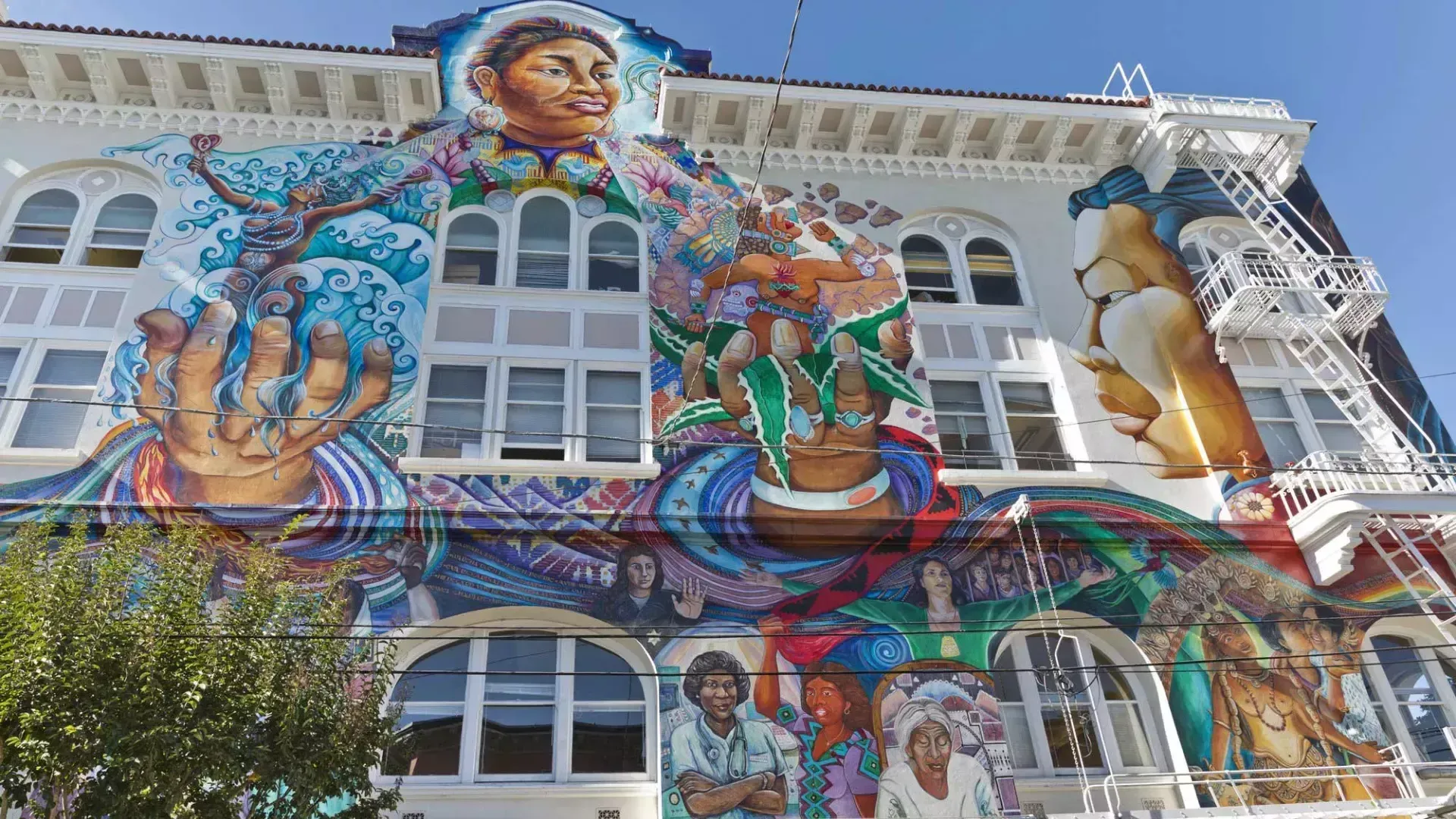 Colorful mural on a building facade with a woman, flowers, birds, and blue wave-like patterns
