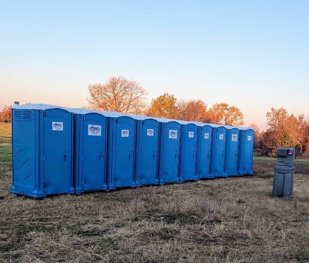 Row of blue portable toilets on a grassy field at sunset