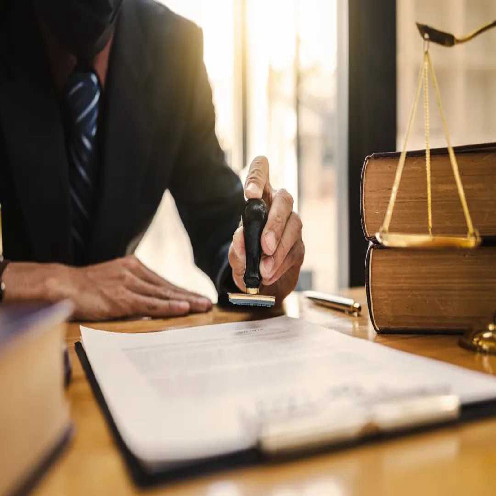 Lawyer stamping documents at a desk beside a scale and stacked legal books