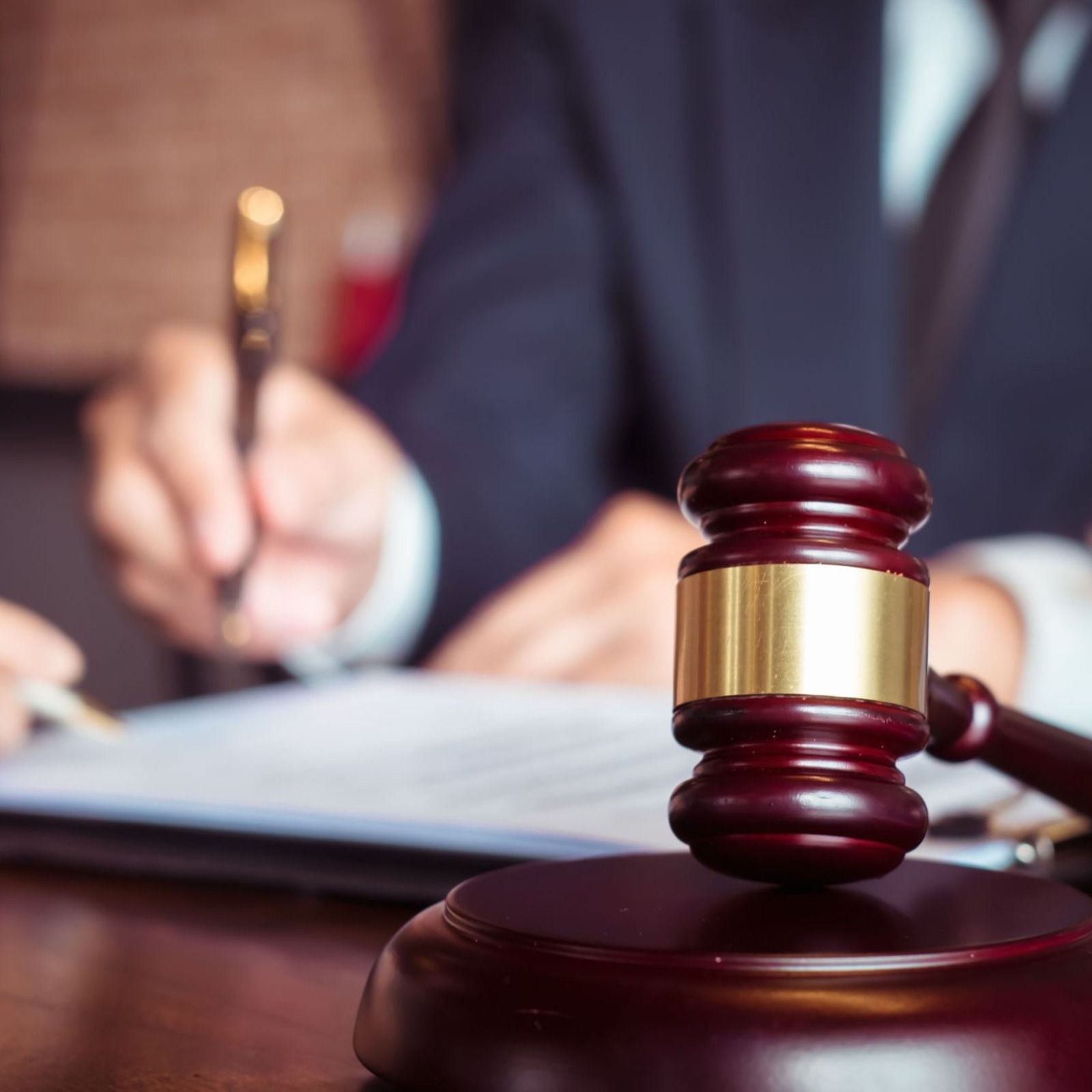 Judge’s gavel on a wooden desk with a blurred lawyer taking notes in the background