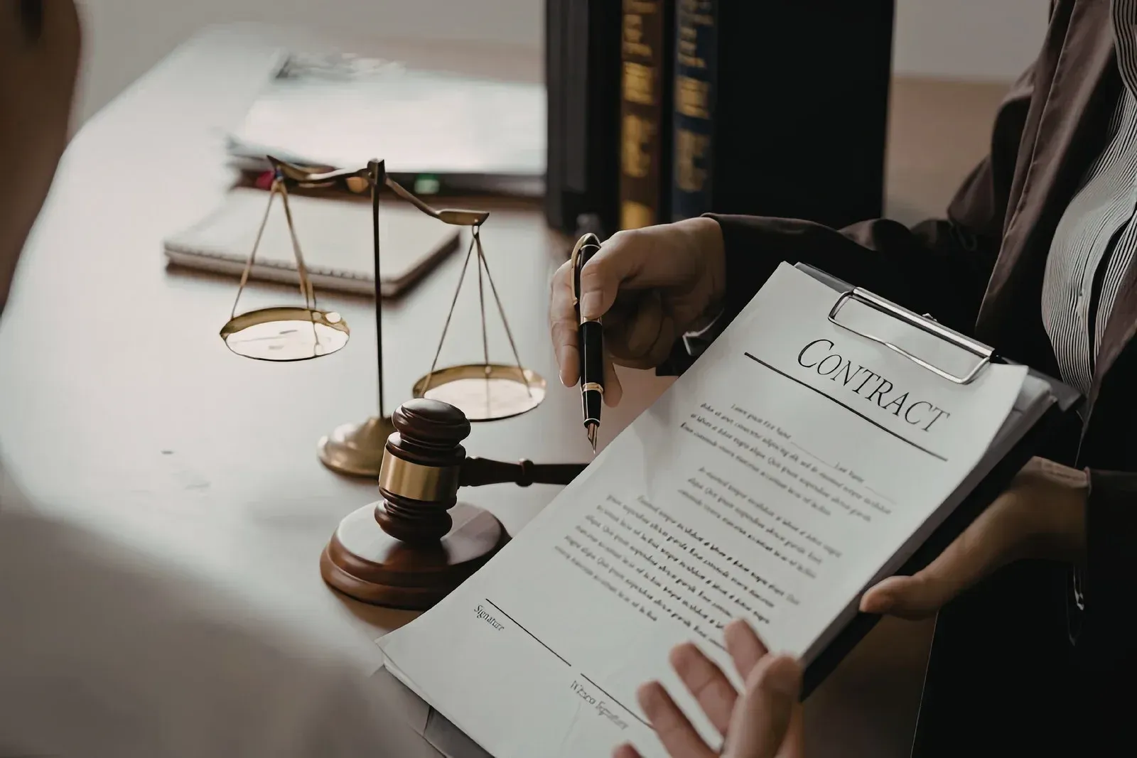 A person presenting a contract to another person with a gavel and a scale of justice on the table in a professional setting.