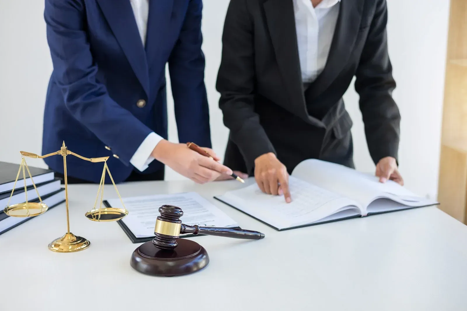 Two people in suits reviewing documents at a table with a gavel, scales of justice, and law books.