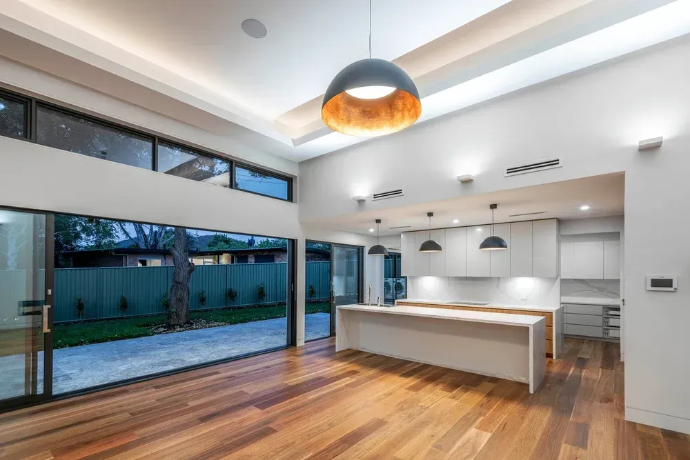 A bright, modern open-plan kitchen with white cabinetry, a large central island, and floor-to-ceiling glass sliding doors.