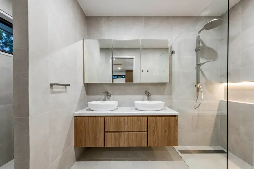 Modern bathroom with double vanity, large mirror, and glass-enclosed shower in beige and wood tones