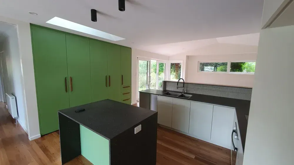 A modern kitchen featuring a dark island, light grey base cabinets, and a wall of bright green floor-to-ceiling cupboards.