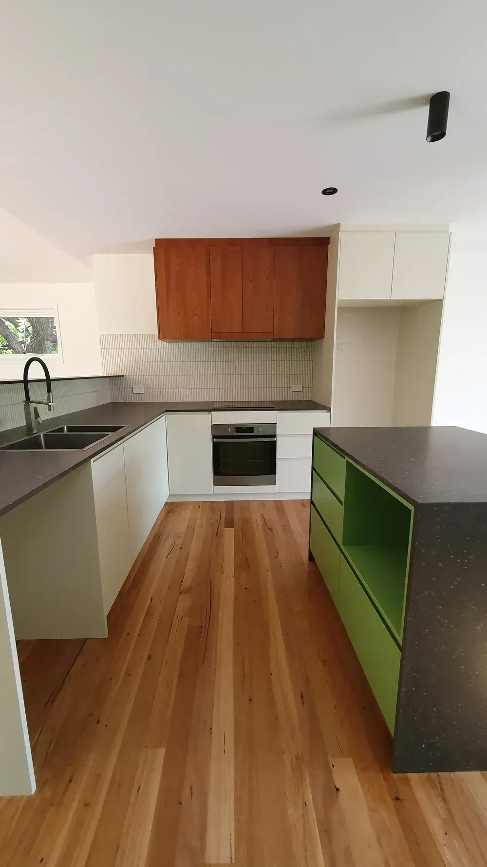 A modern kitchen featuring light green island cabinetry, white lower cabinets, wood-toned upper cabinets, and wood flooring.