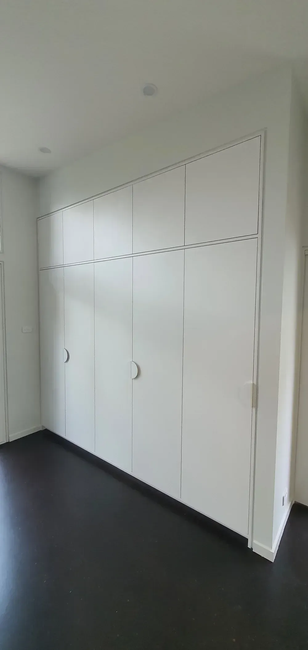 White floor-to-ceiling built-in storage cabinets with dark wood flooring in a minimalist room.
