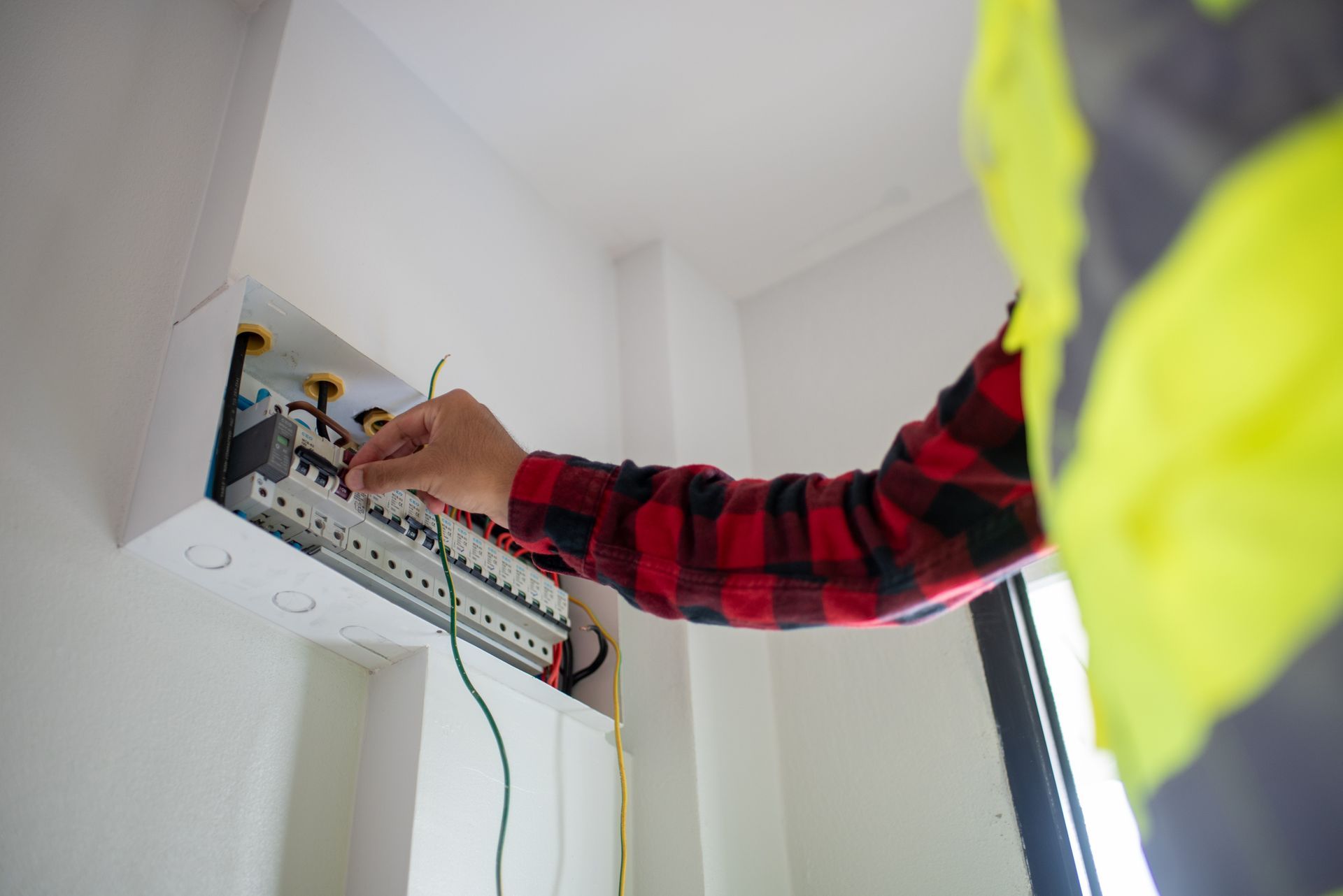 Electrician in a safety vest working on a circuit breaker panel.