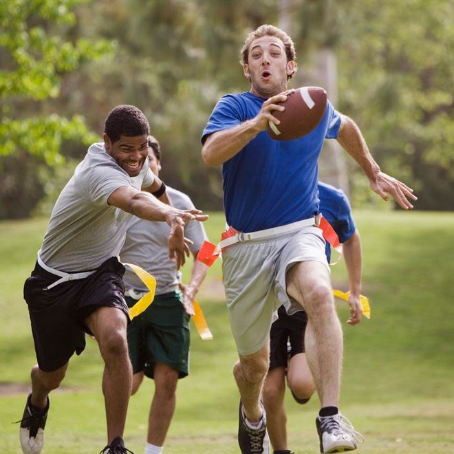 Two athletes sprinting after a football, one in blue catching a pass on a grassy field