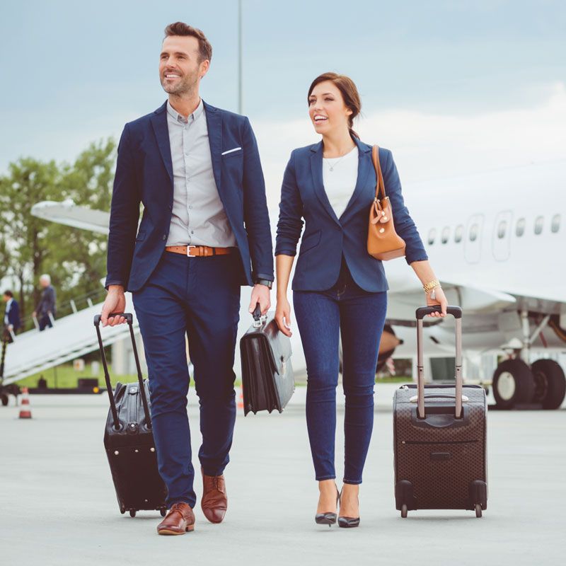 Two business travelers walking with luggage on an airport tarmac near a plane