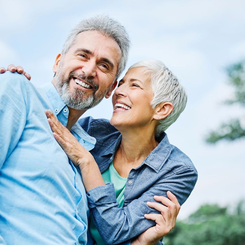 Two smiling people embracing outdoors against a bright blue sky