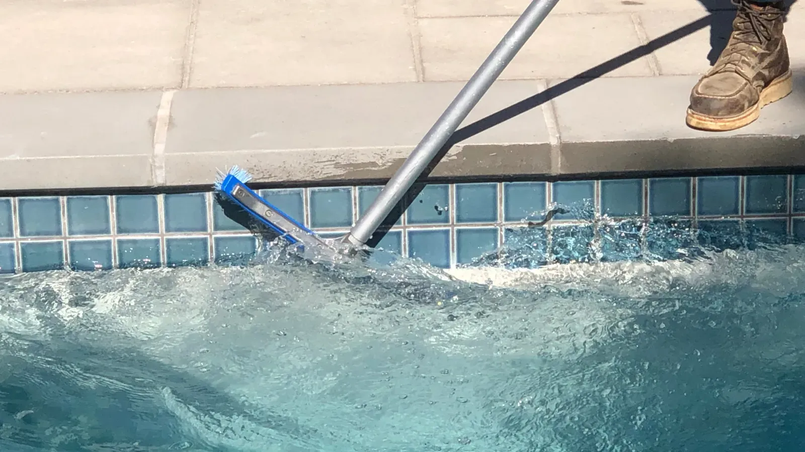 A person is cleaning a swimming pool with a vacuum cleaner.