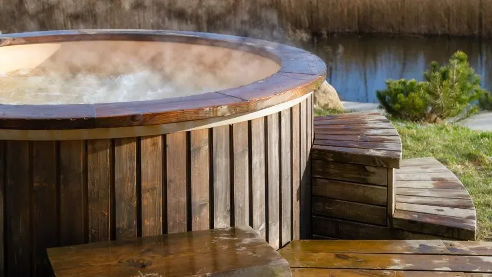 A wooden hot tub is sitting on a wooden deck next to a body of water.