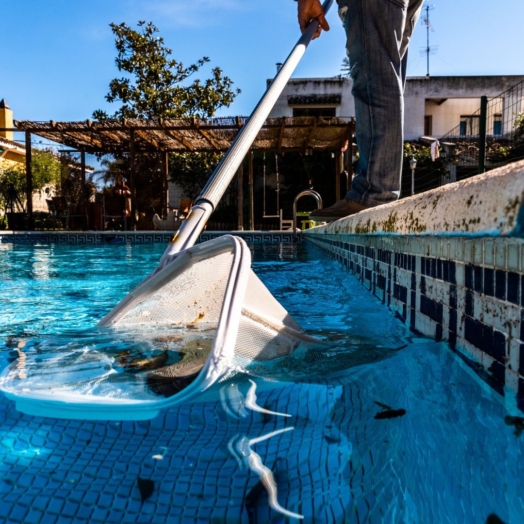 A person is cleaning a swimming pool with a vacuum cleaner