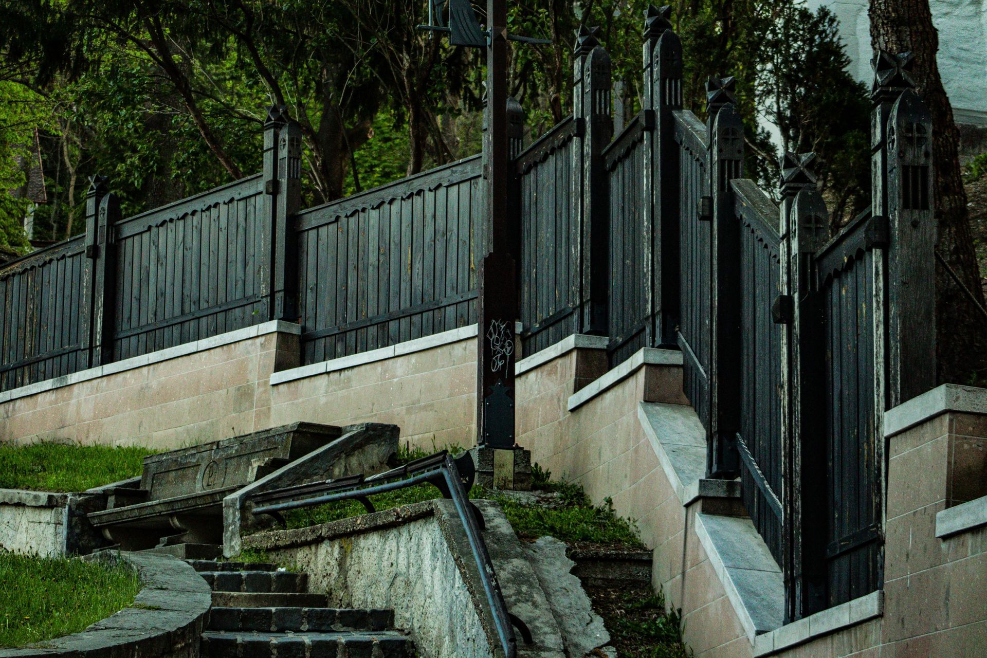 Steep outdoor stairway with concrete retaining walls and dark metal fencing beside trees