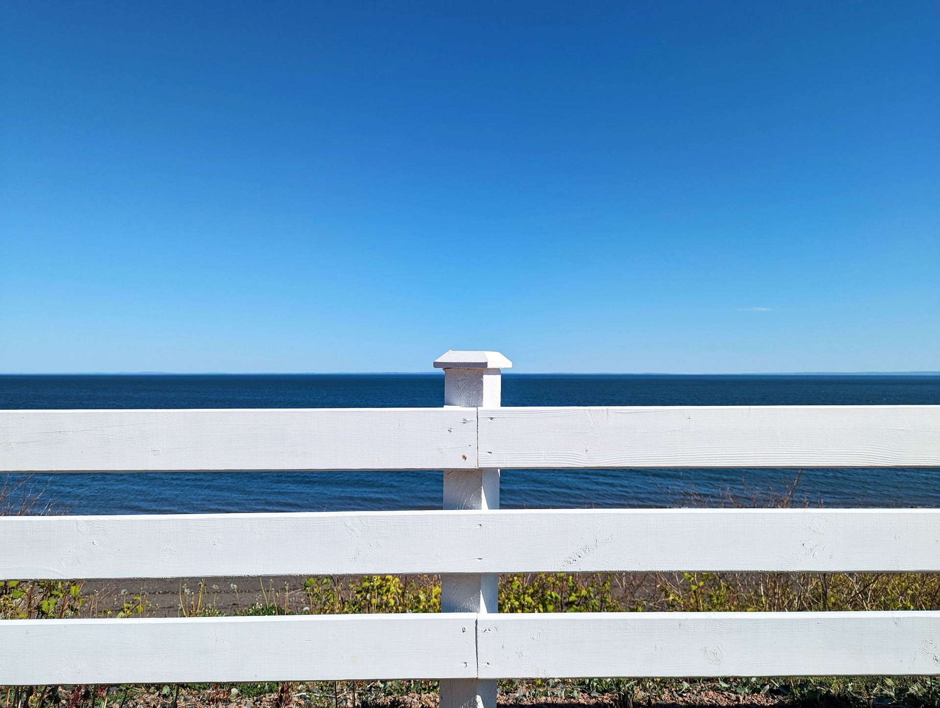 White wooden fence overlooking a calm blue ocean under a clear sky
