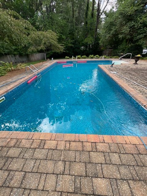 A large swimming pool is surrounded by trees and a brick patio.