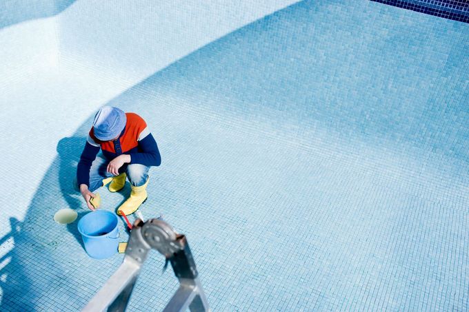 A person is cleaning a swimming pool with buckets and sponges.
