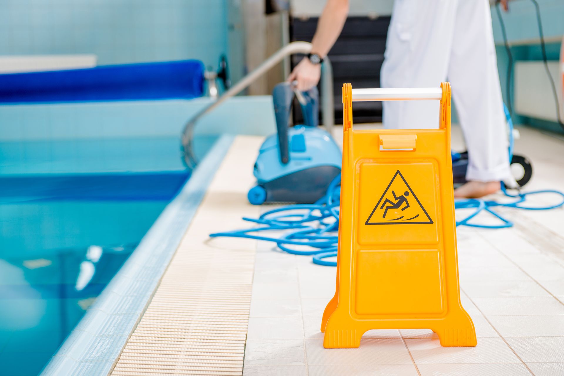 A yellow wet floor sign is next to a swimming pool.
