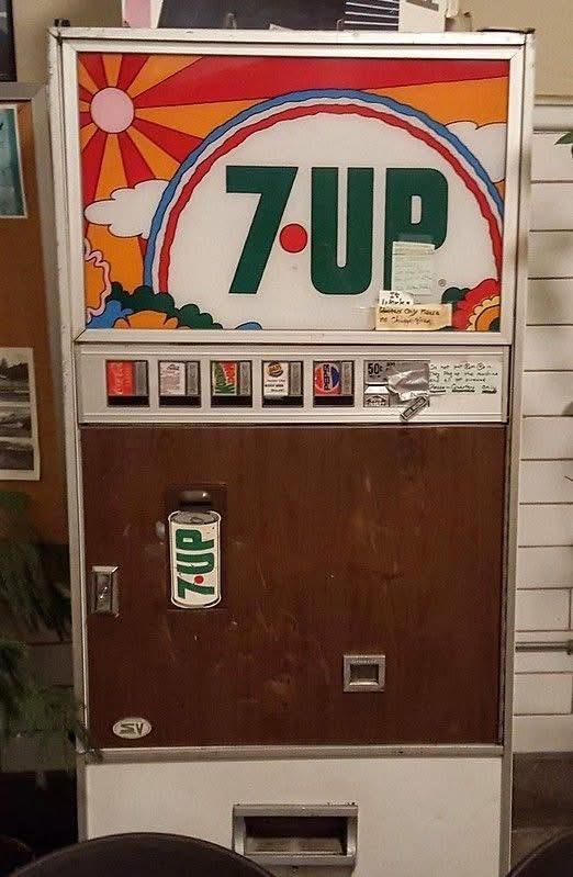 Vintage 7-Up vending machine with groovy floral and sun design on top panel, brown cabinet, and a 7-Up can logo.