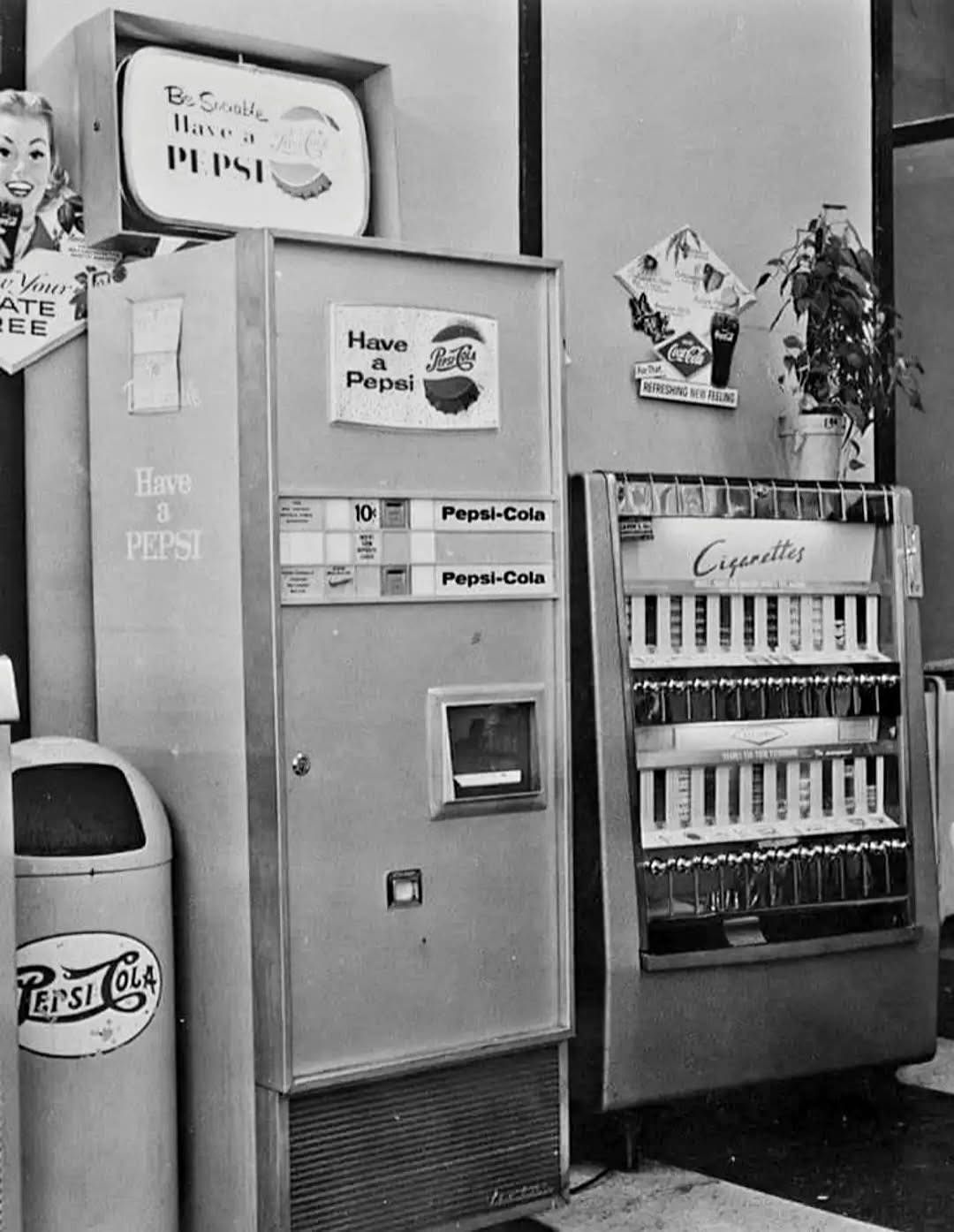 Vintage Pepsi and cigarette vending machines. Indoor shot with a trash can and posters.