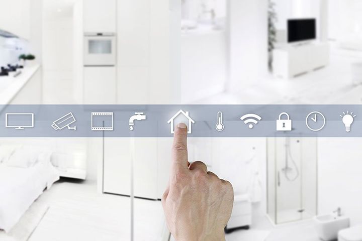 Mano che indica l'icona di una casa sul pannello di controllo di una casa intelligente, con uno sfondo interno bianco.
