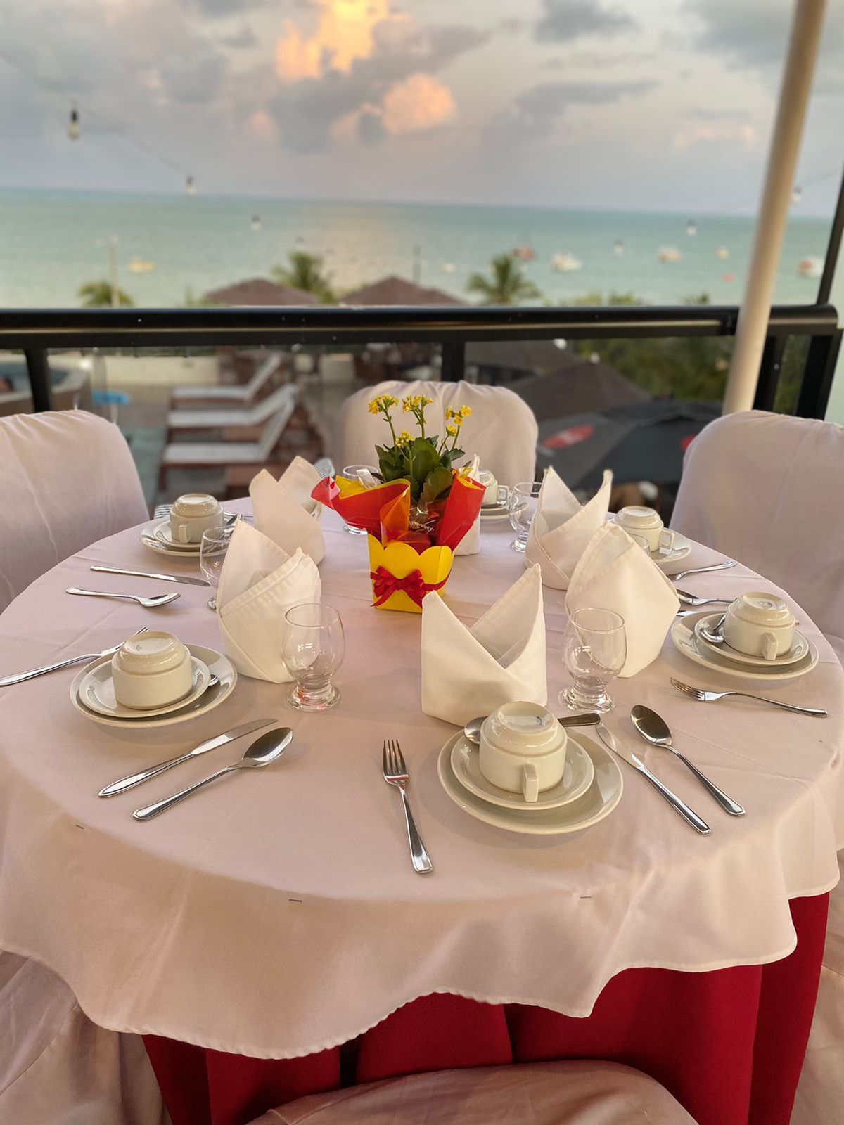 Uma mesa redonda posta para quatro pessoas, com toalhas de mesa brancas e vista para o mar ao fundo.