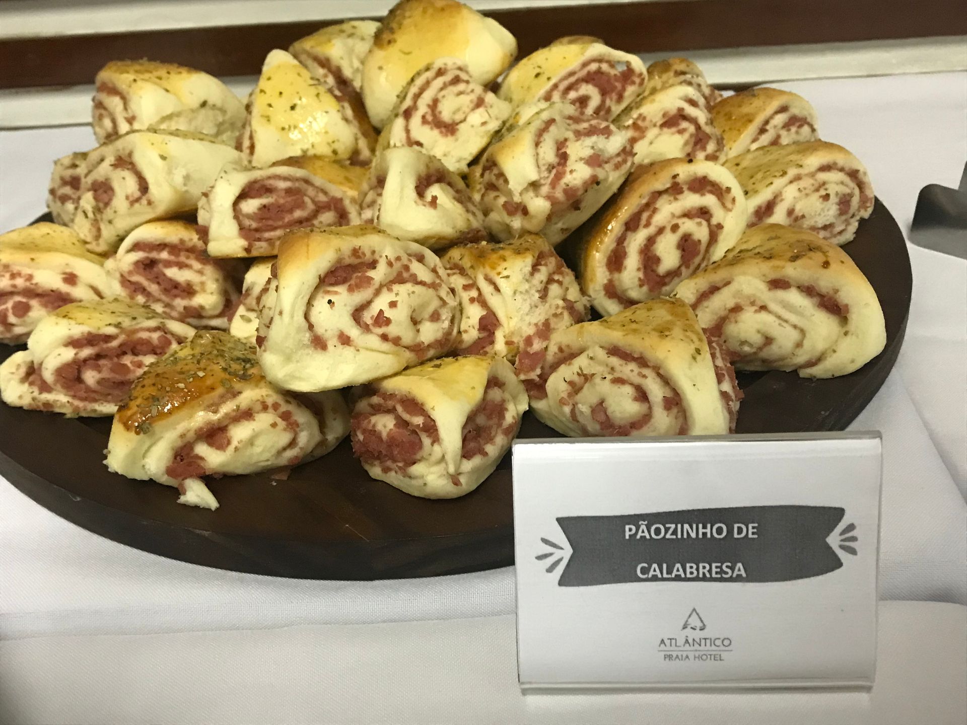 Uma travessa de madeira repleta de pequenos pastéis salgados em formato espiral, com a etiqueta 