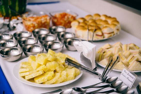 Uma mesa de bufê com um prato de abacaxi fatiado, tigelas pequenas, pãezinhos e sanduíches triangulares.