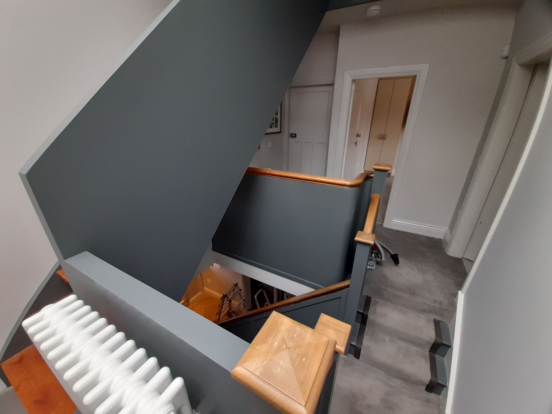 Stairwell with a folded stairlift beside a landing, gray walls, and a white radiator in the foreground