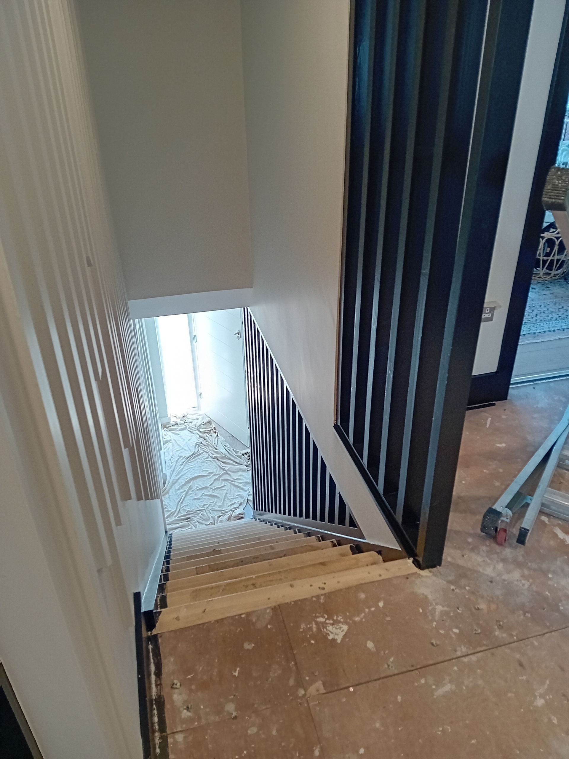 Stairwell with beige steps, white walls, dark blue railing, and daylight at the bottom.