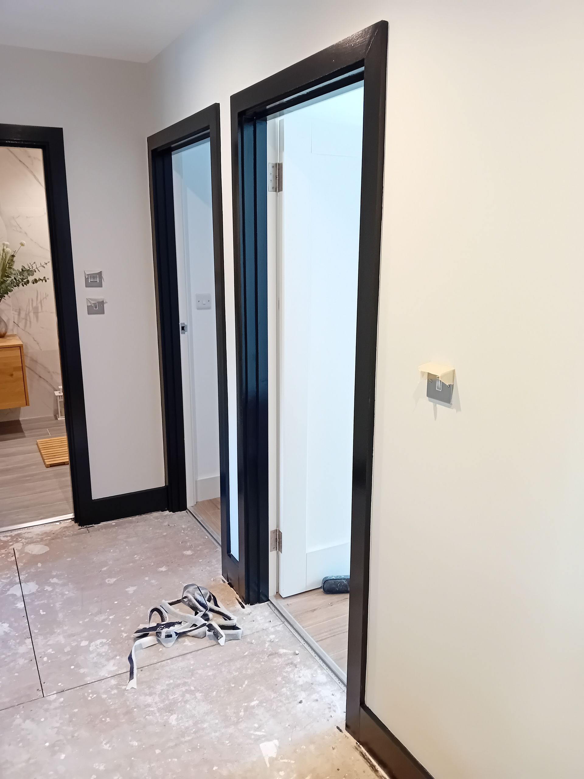 Empty hallway with two open doorways, black trim, and construction debris on the floor.