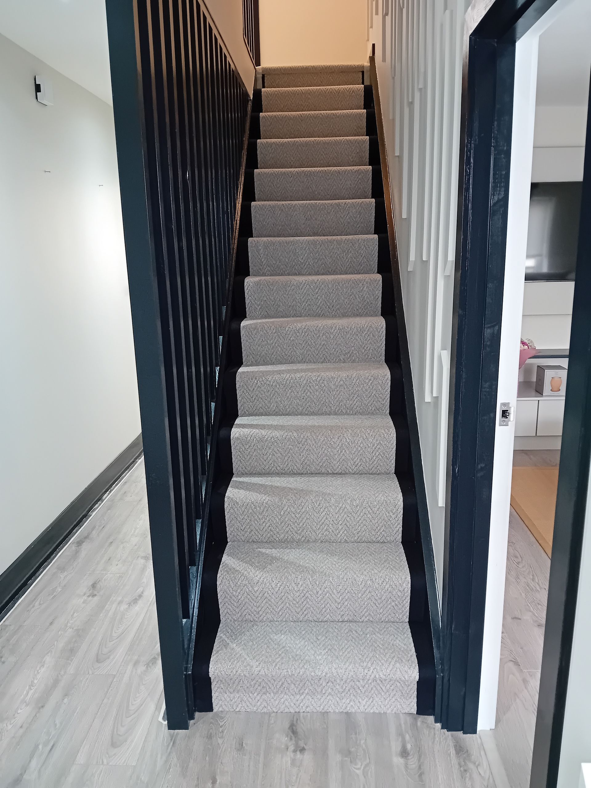 Narrow carpeted staircase with black railing in a hallway, leading upstairs.