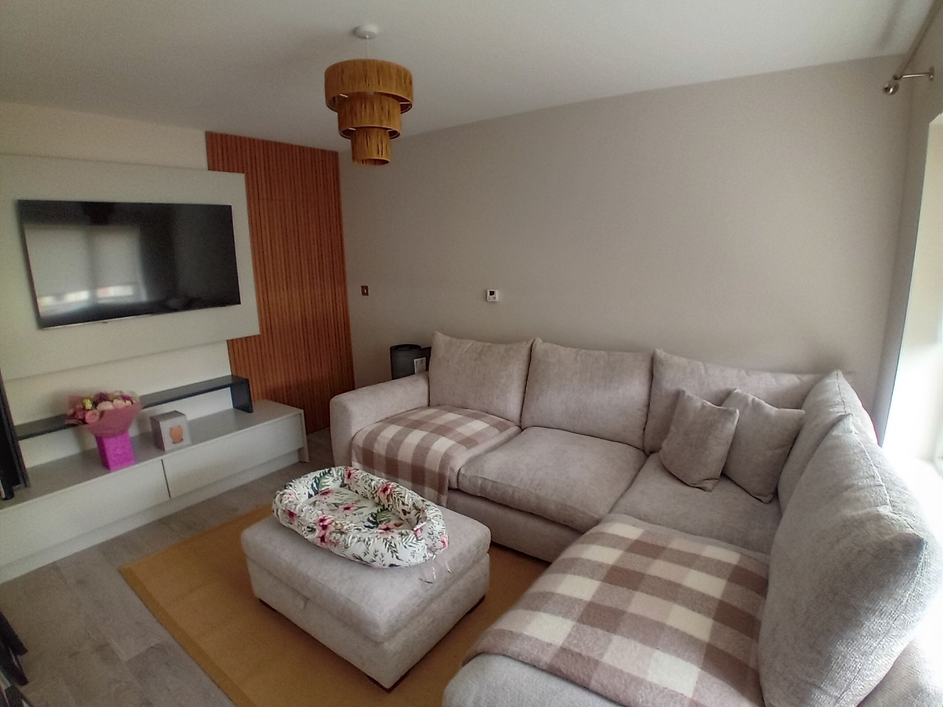 Modern living room with gray sectional sofa, ottoman, wall-mounted TV, and plaid throw blanket