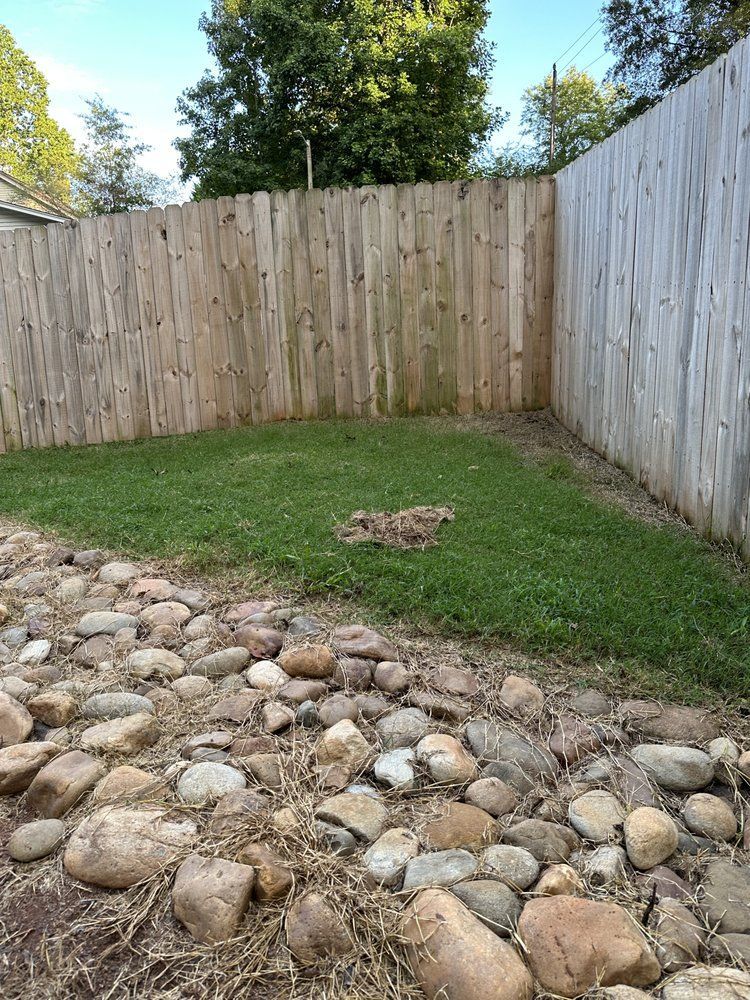 A small backyard with a grass patch surrounded by a wooden fence and rocks.