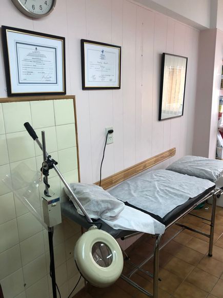 Sala de tratamiento de la clínica con camilla de exploración, silla de ruedas, certificados enmarcados y equipo médico.