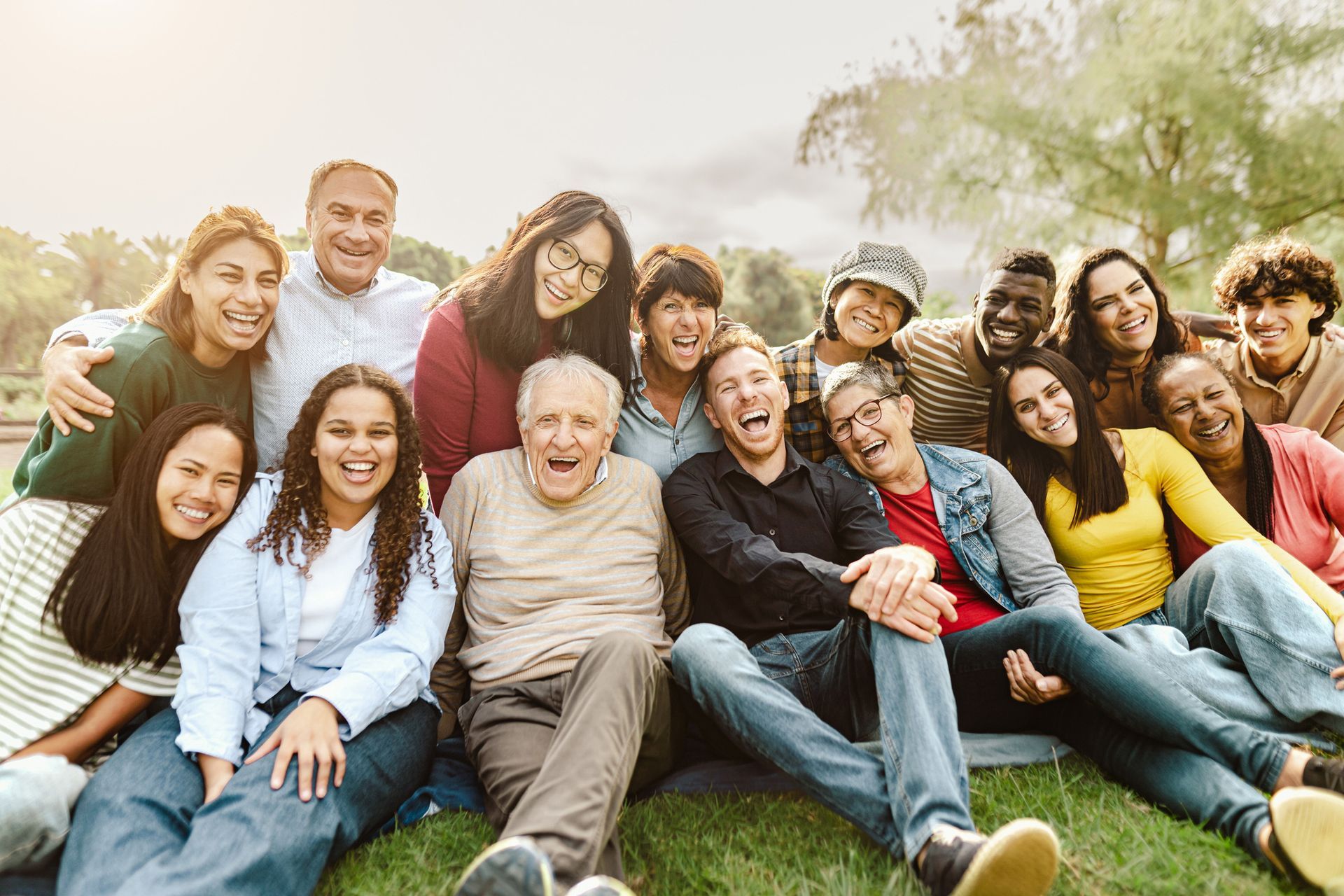 Group of diverse people smiling and laughing outdoors, on the grass.