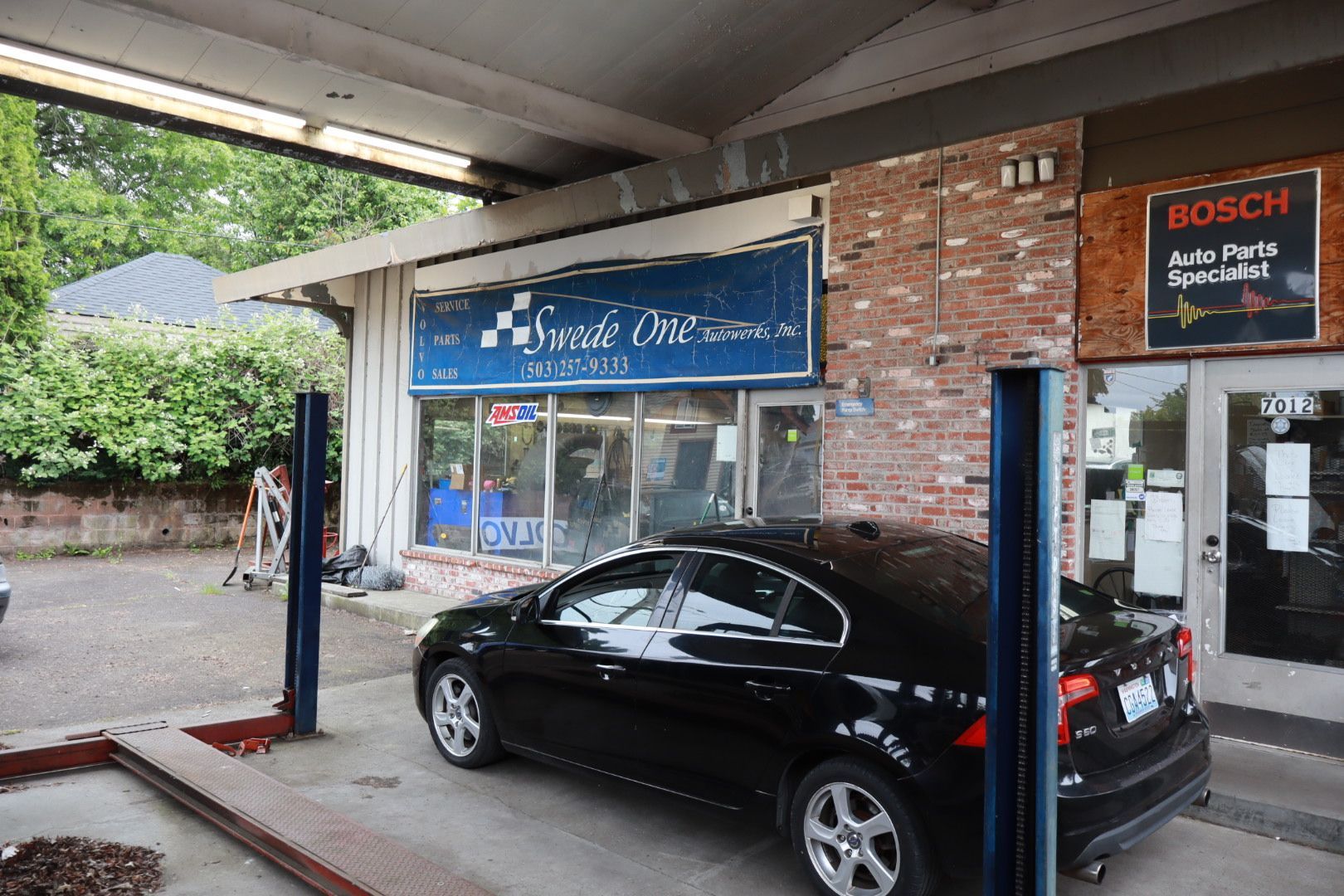 Black car parked outside a small shop with a blue sign and BOSCH auto service on the right