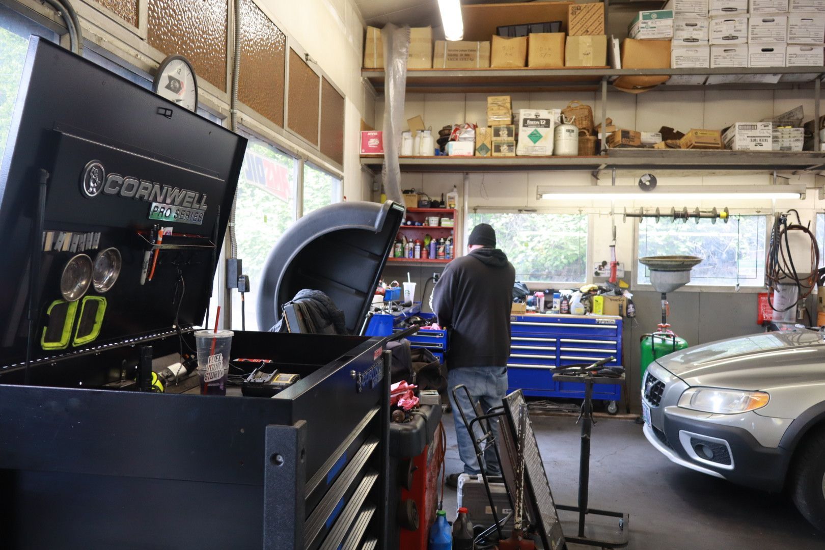Auto repair garage with a mechanic, toolboxes, shelves, and a car in a service bay