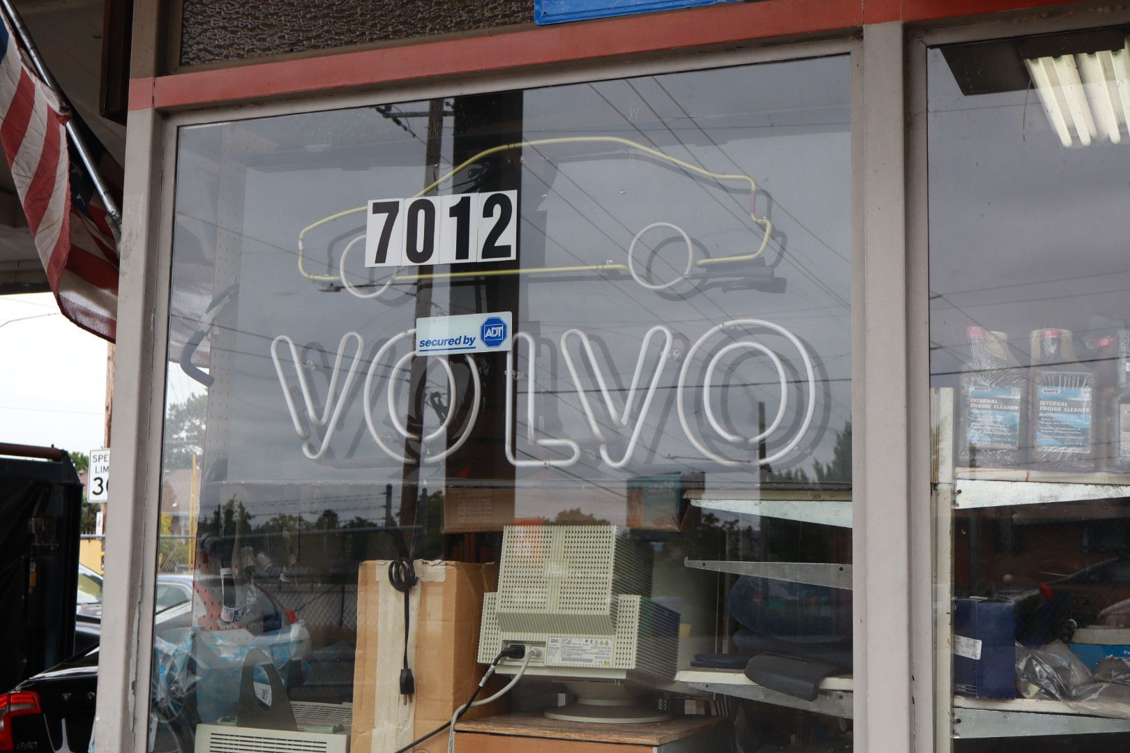 Volvo dealership storefront with glass windows, sign number 7012, and parked vehicles reflected inside