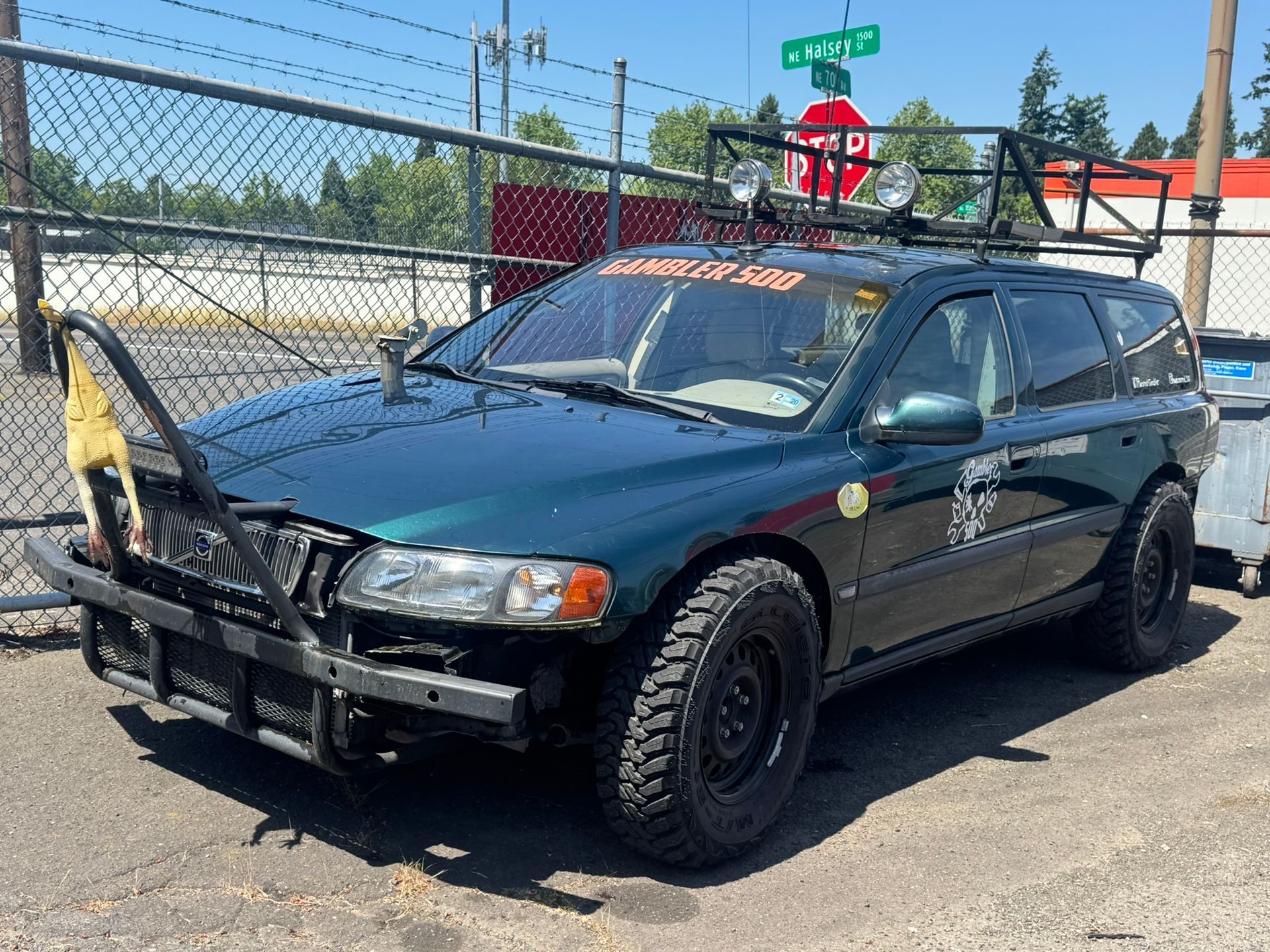 Dark blue SUV with a front-mounted bull bar parked by a chain-link fence on a sunny street.