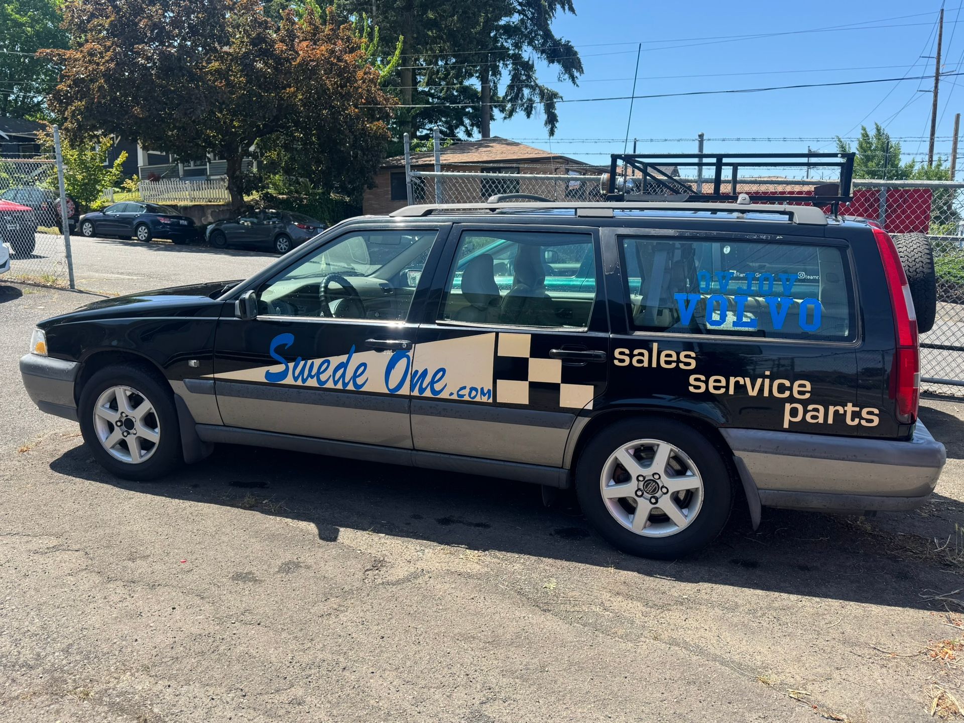 Black hatchback with “Speed One” and “sales service parts” decals parked in a lot under a blue sky