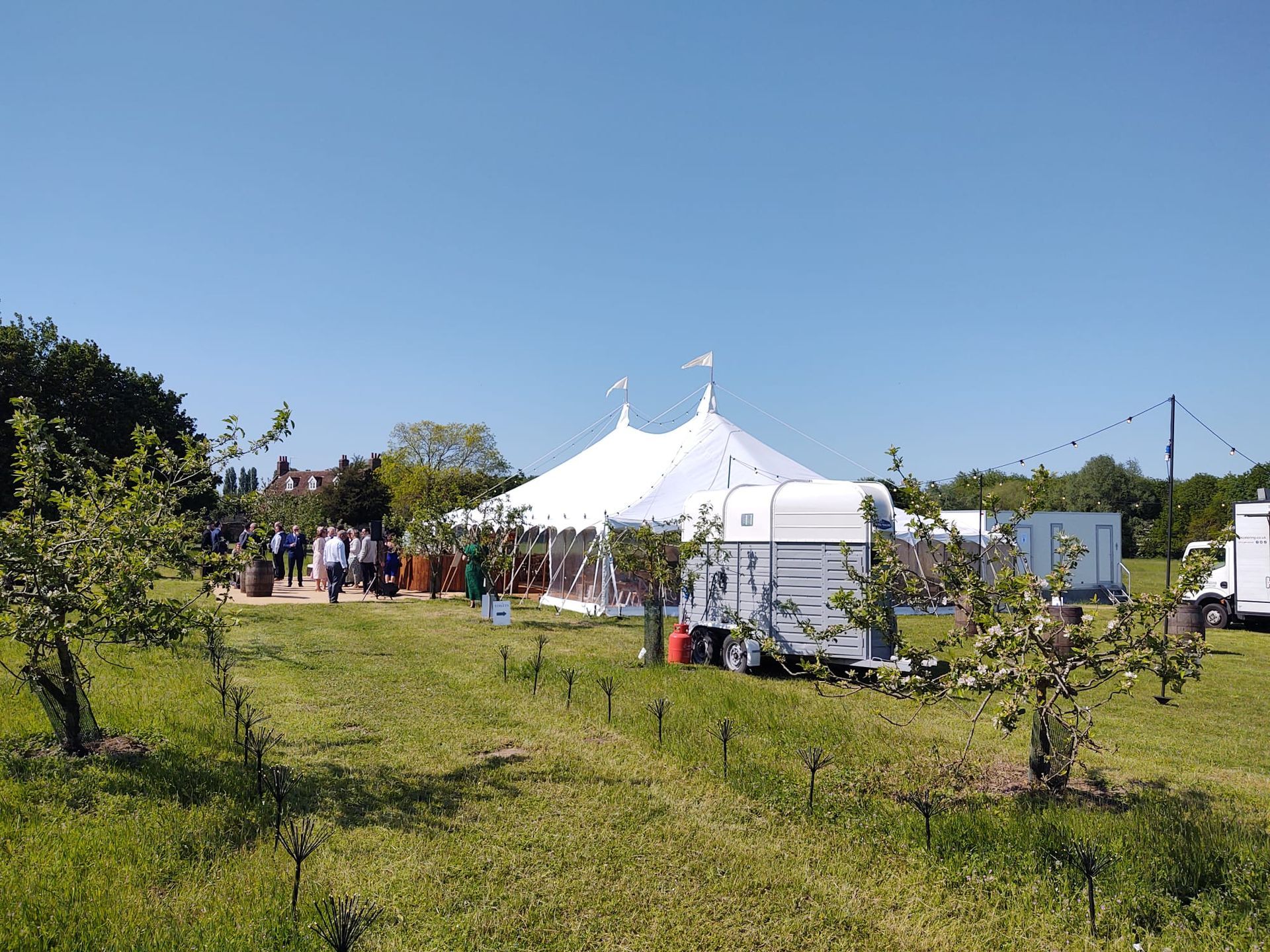 White event tent on a grassy hill with a small crowd under a clear blue sky