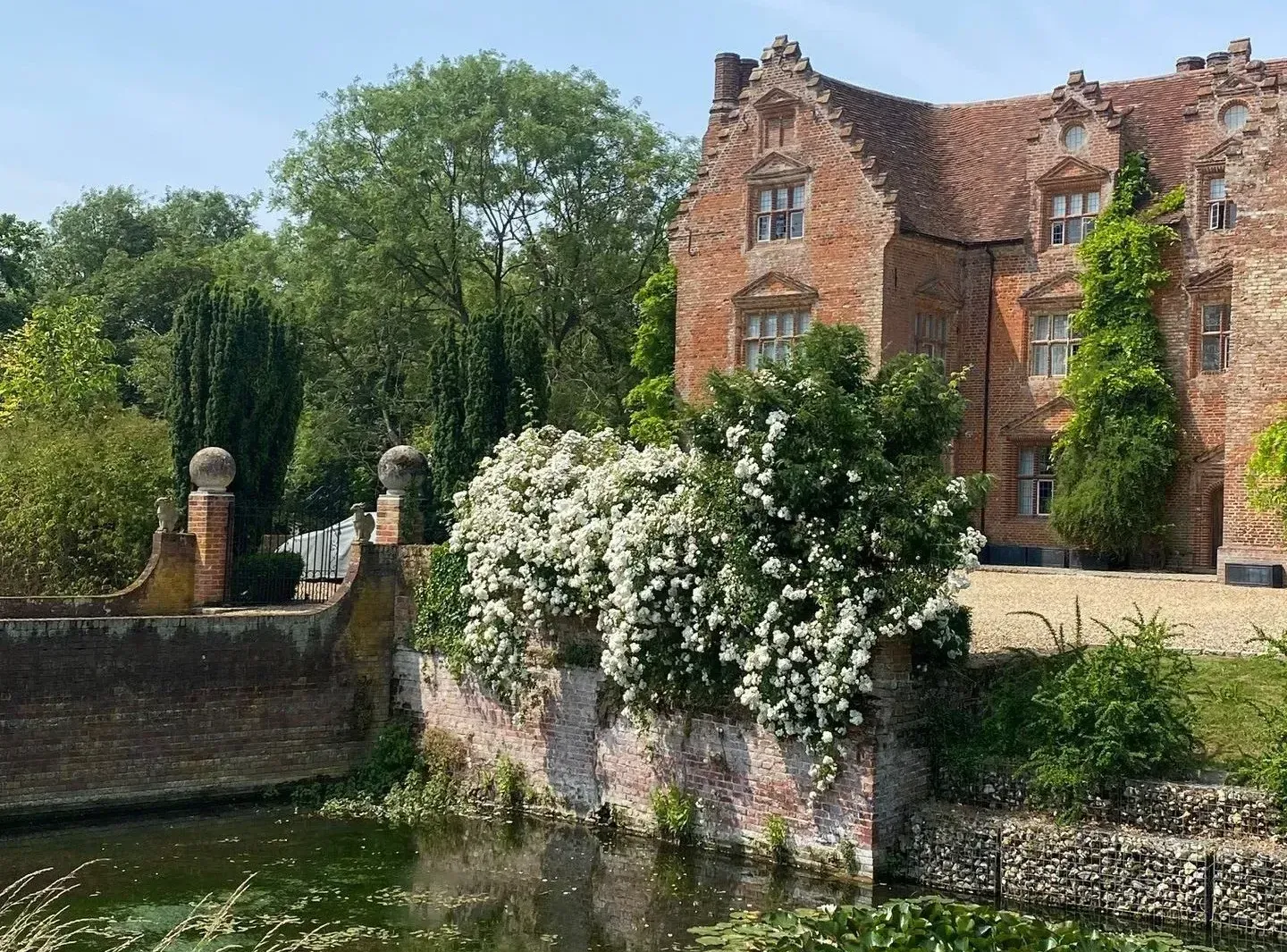 Brick cottage beside a stone bridge and flower-lined canal in a sunny garden