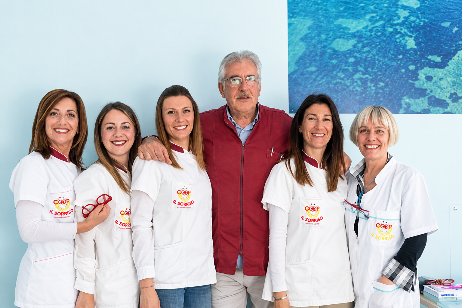 Gruppo di sei persone con camicie bianche e una con giacca rossa, in piedi insieme in un ambiente interno